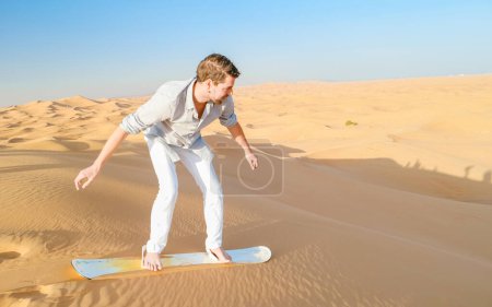 Foto de Young men sand surfing at the sand dunes of Dubai United Arab Emirates, sand desert on a sunny day in Dubai. - Imagen libre de derechos