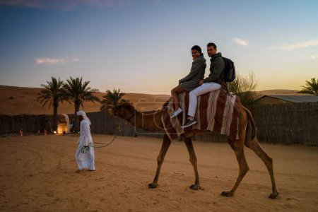 Téléchargez les photos : Couple riding a camel during Dubai desert safari at the safari camp, Dubai United Arab Emirates - en image libre de droit