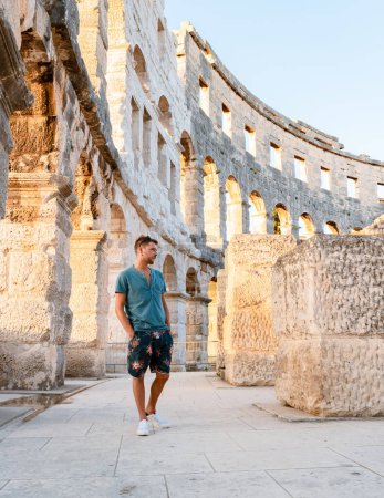 Photo for Young men tourists visit Pula city in Croatia, Roman Amphi theatre Arena in Pula on a bright summer day evening, A wall fragment of ancient Roman amphitheater Coliseum PulaPula, Croatia. - Royalty Free Image