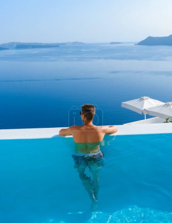 Téléchargez les photos : Man relaxing in infinity swimming during vacation at Santorini, swimming pool looking out over the Caldera ocean of Santorini, Oia Greece, Greek Island Aegean Cyclades luxury vacation. - en image libre de droit