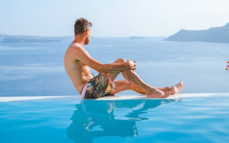 Téléchargez les photos : Homme relaxant à l'infini nageant pendant les vacances à Santorin, piscine donnant sur l'océan Caldera de Santorin, Oia Grèce, île grecque Cyclades égéennes vacances de luxe. - en image libre de droit
