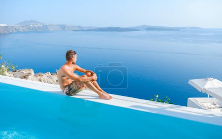 Foto de Young man relaxing in infinity swimming during vacation at Santorini, swimming pool looking out over the Caldera ocean of Santorini, Oia Greece, Greek Island Aegean Cyclades luxury vacation. - Imagen libre de derechos