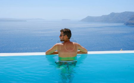 Téléchargez les photos : Young man relaxing in infinity swimming during vacation at Santorini, swimming pool looking out over the Caldera ocean of Santorini, Oia Greece, Greek Island Aegean Cyclades luxury vacation. - en image libre de droit