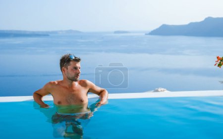 Téléchargez les photos : Man relaxing in infinity swimming pool during vacation at Santorini, swimming pool looking out over the Caldera ocean of Santorini, Oia Greece, Greek Island Aegean Cyclades luxury vacation. - en image libre de droit