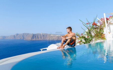 Foto de Men relaxing in an infinity swimming pool during vacation at Santorini, swimming pool looking out over the Caldera ocean of Santorini, Oia Greece, Greek Island Aegean Cyclades luxury vacation. - Imagen libre de derechos