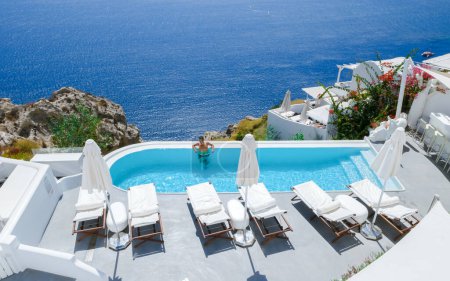 Téléchargez les photos : Men relaxing in an infinity swimming pool during vacation at Santorini, swimming pool looking out over the Caldera ocean of Santorini, Oia Greece, Greek Island Aegean Cyclades luxury vacation. - en image libre de droit