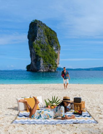 Téléchargez les photos : Koh Poda Beach Krabi Thaïlande, la plage tropicale de Koh Poda Krabi, un couple d'hommes et de femmes sur la plage pique-nique avec des fruits et boissons - en image libre de droit