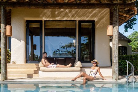 Téléchargez les photos : Hommes travaillant sur un ordinateur portable un nomade numérique travaillant dans une piscine pendant des vacances sur une île tropicale. homme et femme dans la piscine à débordement au coucher du soleil. vacances de luxe dans une villa piscine de luxe - en image libre de droit
