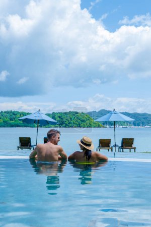 Téléchargez les photos : Un jeune couple d'hommes et de femmes dans une piscine pendant des vacances sur une île tropicale. homme et femme dans la piscine à débordement au coucher du soleil. vacances de luxe dans une villa piscine de luxe - en image libre de droit
