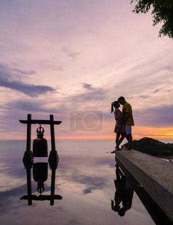 Téléchargez les photos : Romantic couple of men and women at a swimming pool during a vacation on a tropical island. man and woman in the infinity pool during sunset. luxury vacation in a luxury pool villa - en image libre de droit