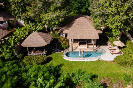 Téléchargez les photos : Vue de drone d'en haut à un jeune couple d'hommes et de femmes à une piscine pendant des vacances sur une île tropicale. homme et femme dans la piscine à débordement, - en image libre de droit
