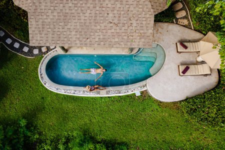 Téléchargez les photos : Drone view from above at a young couple of men and women at a swimming pool during a vacation on a tropical island. man and woman in the infinity pool, luxury vacation in a luxury pool villa - en image libre de droit