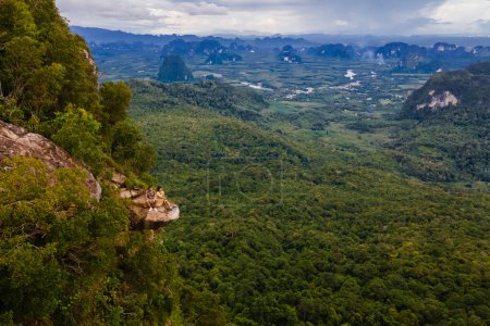 Photo for Couple at the edge of a mountain, Dragon Crest mountain Krabi Thailand, Young travelers sits on a rock that overhangs the abyss, with a beautiful landscape. Dragon Crest or Khuan Sai at Khao Ngon Nak - Royalty Free Image