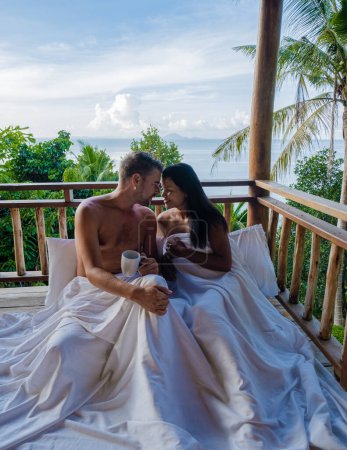 Téléchargez les photos : Couple se réveillant au lit dans une jungle naturelle regardant au-dessus de l'océan au lever du soleil, dans une cabane en bois dans les montagnes de Thaïlande Asie Phangnga Bay - en image libre de droit