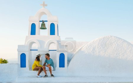 Foto de Young couple of men and women tourists visit Oia Santorini Greece on a sunny day during summer with whitewashed homes and churches, Greek Island Aegean Cyclades - Imagen libre de derechos