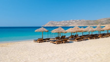 Téléchargez les photos : Mykonos plage pendant l'été avec parasol et chaises longues de luxe lits, océan bleu avec la montagne à Elia plage Mikonos Grèce. - en image libre de droit