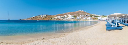 Foto de Mykonos beach during summer with umbrella and luxury beach chairs beds, blue ocean with the mountain at Elia beach Mikonos Greece. - Imagen libre de derechos