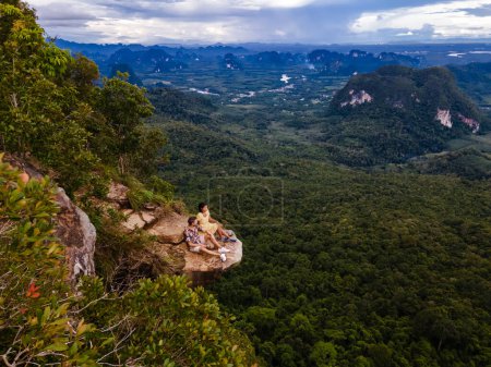Téléchargez les photos : Couple hommes et femmes au bord d'une montagne, Dragon Crest montagne Krabi Thaïlande, Jeunes voyageurs assis sur un rocher qui surplombe l'abîme, Dragon Crest ou Khuan Sai à Khao Ngon Nak - en image libre de droit