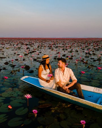 Téléchargez les photos : Lever de soleil à la mer de lotus rouge, lac Nong Harn, Udon Thani, Thaïlande. Couple d'hommes et de femmes dans un bateau en bois au lever du soleil au lac de lotus rouge en Thaïlande - en image libre de droit