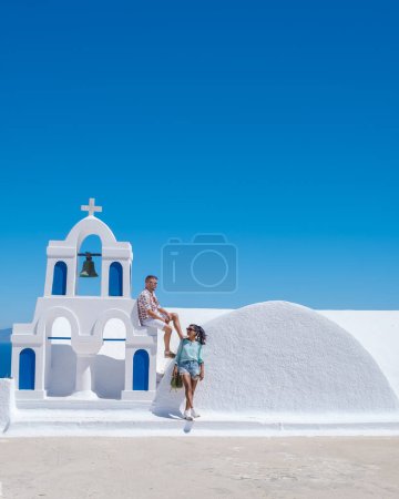 Téléchargez les photos : Visite de couple Santorin Grèce, hommes et femmes visitent le village grec blanchi à la chaux d'Oia pendant les vacances d'été au lever du soleil sur les dômes bleus et les églises blanches - en image libre de droit