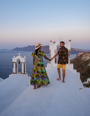 Téléchargez les photos : Couple regardant le coucher du soleil en vacances à Santorin en Grèce, hommes et femmes regardant le village avec des églises blanches et des dômes bleus en Grèce. - en image libre de droit