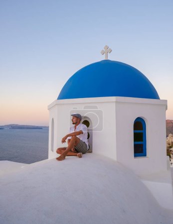 Photo for Young men watching the sunrise in Santorini Greece, man on vacation at the Greek village Oia with whitewashed house and churches. - Royalty Free Image