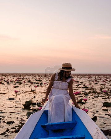Foto de Asian women with a hat and dress in a boat at the Beautiful Red Lotus Sea Kumphawapi is full of pink flowers in Udon Thani in northern Thailand. Flora of Southeast Asia. - Imagen libre de derechos