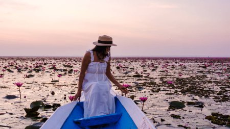 Téléchargez les photos : Femmes asiatiques avec un chapeau et une robe dans un bateau à la Belle Mer Rouge Lotus Kumphawapi est plein de fleurs roses à Udon Thani dans le nord de la Thaïlande. Flore de l'Asie du Sud-Est. - en image libre de droit