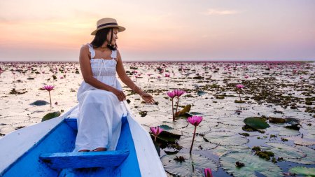 Foto de Mujeres asiáticas con sombrero y vestido en un barco en el hermoso mar de loto rojo Kumphawapi está lleno de flores rosadas en Udon Thani en el norte de Tailandia. Flora del Sudeste Asiático. - Imagen libre de derechos