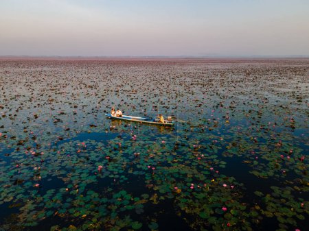 Photo for Couple in a wooden boat at the Beautiful Red Lotus Sea Kumphawapi is full of pink flowers in Udon Thani in northern Thailand. Flora of Southeast Asia. - Royalty Free Image