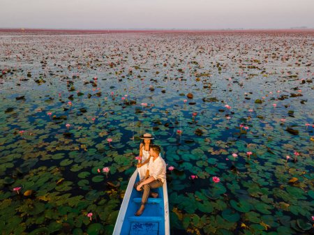 Téléchargez les photos : Couple dans un bateau en bois à la Belle Mer Rouge Lotus Kumphawapi est plein de fleurs roses à Udon Thani dans le nord de la Thaïlande. Flore de l'Asie du Sud-Est. - en image libre de droit