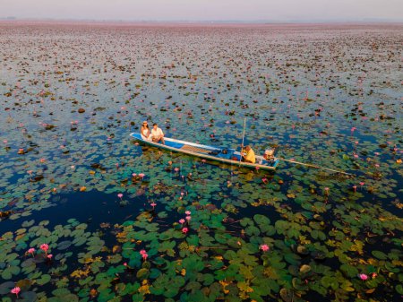 Téléchargez les photos : Couple dans un bateau en bois à la Belle Mer Rouge Lotus Kumphawapi est plein de fleurs roses à Udon Thani dans le nord de la Thaïlande. Flore de l'Asie du Sud-Est. - en image libre de droit