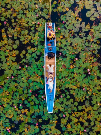 Foto de Pareja en un barco de madera en el hermoso mar de loto rojo Kumphawapi está lleno de flores rosadas en Udon Thani en el norte de Tailandia. Flora del Sudeste Asiático. - Imagen libre de derechos
