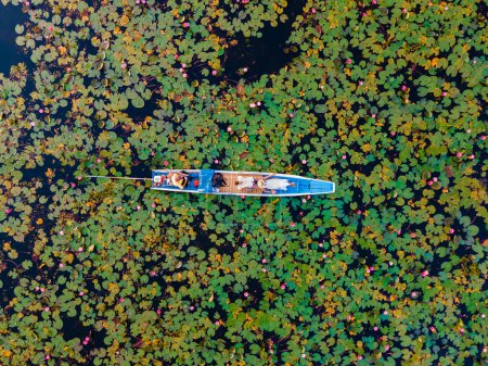 Téléchargez les photos : Couple d'hommes et de femmes dans un bateau en bois à la Belle Mer Rouge Lotus Kumphawapi est plein de fleurs roses à Udon Thani dans le nord de la Thaïlande. Flore de l'Asie du Sud-Est. - en image libre de droit
