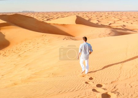 Foto de Jóvenes caminando en el desierto de Dubai, Dunas de arena de Dubai Emiratos Árabes Unidos, desierto de arena en un día soleado en Dubai. - Imagen libre de derechos