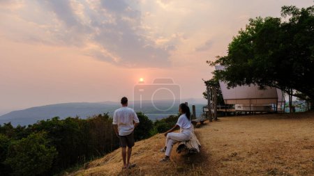 Téléchargez les photos : Un couple d'hommes et de femmes regardant le coucher du soleil dans un camping de montagne à Phitsanulok Thaïlande. glamping de luxe en montagne nature - en image libre de droit