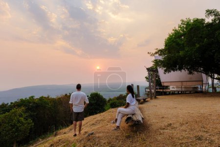 Téléchargez les photos : Un couple d'hommes et de femmes regardant le coucher du soleil dans un camping de montagne à Phitsanulok Thaïlande. glamping de luxe - en image libre de droit
