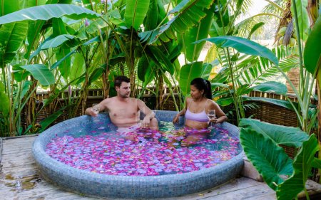 Photo for Couple at a bathtub in the rainforest of Thailand during a vacation with flowers in the bath, men and women relaxing in a jacuzzi with rose petals outside in nature. - Royalty Free Image