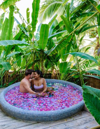 Téléchargez les photos : Couple dans une baignoire dans la forêt tropicale de Thaïlande pendant des vacances avec des fleurs dans le bain, les hommes et les femmes se détendre dans un jacuzzi avec des pétales de rose à l'extérieur dans la nature. - en image libre de droit