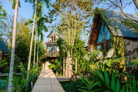 Foto de Casa de madera rodeada de palmeras y un huerto en el campo. cabaña en selva tropical - Imagen libre de derechos