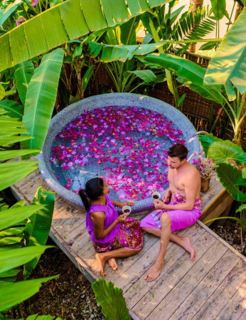Foto de Pareja relajándose en una bañera en la selva tropical de Tailandia durante unas vacaciones con flores en el baño, hombres y mujeres relajándose en un jacuzzi con pétalos de rosa en la naturaleza. - Imagen libre de derechos