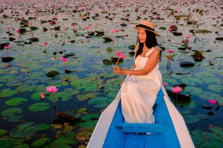 Foto de Las mujeres tailandesas en el mar de loto rojo, Lago Nong Harn, Udon Thani, Tailandia, mujer asiática con un vestido y sombrero en un barco de madera en el lago de loto rojo. - Imagen libre de derechos