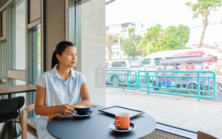 Photo for Asian women drinking coffee in a cafe in Bangkok Thailand with a look at the streets. - Royalty Free Image