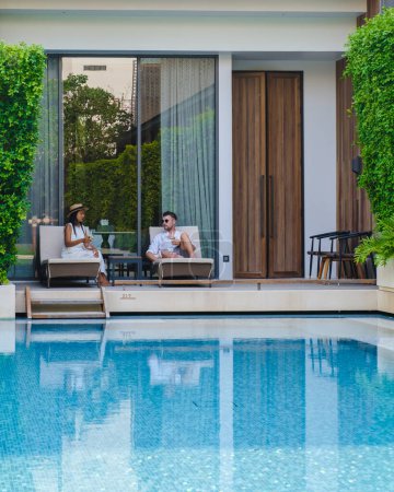 Téléchargez les photos : Luxe hôtel 5 étoiles piscine en Asie. Un couple d'hommes et de femmes en vacances dans un hôtel de luxe, hommes et femmes au bord de la piscine le soir - en image libre de droit