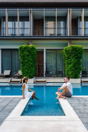 Téléchargez les photos : Luxe hôtel 5 étoiles piscine en Asie. Un couple d'hommes et de femmes en vacances dans un hôtel de luxe, hommes caucasiens et femmes thaïlandaises près de la piscine - en image libre de droit