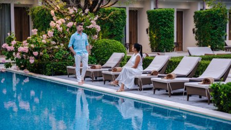 Téléchargez les photos : Luxe hôtel 5 étoiles piscine en Asie. Un couple d'hommes et de femmes en vacances dans un hôtel de luxe, hommes et femmes au bord de la piscine - en image libre de droit