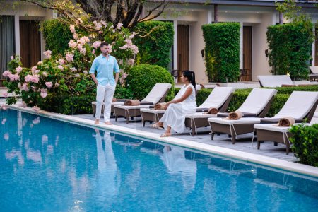 Téléchargez les photos : Luxe hôtel 5 étoiles piscine en Asie. Un couple d'hommes et de femmes en vacances dans un hôtel de luxe, hommes et femmes au bord de la piscine le soir - en image libre de droit