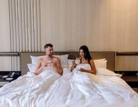 Téléchargez les photos : Couple se réveillant au lit avec café dans la chambre d'un hôtel de luxe. hommes et femmes au lit - en image libre de droit