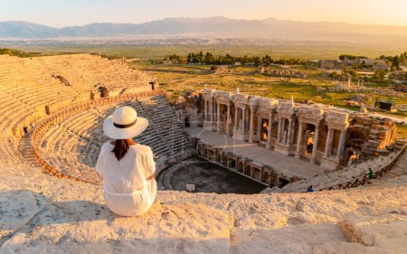 Photo for Hierapolis ancient city Pamukkale Turkey, a young woman with a hat watching the sunset by the ruins Unesco. Asian women watching sunset at the old Amphitheater in Turkey - Royalty Free Image