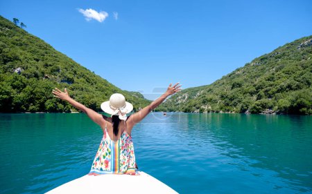 Foto de Una mujer con un sombrero y la mano en el aire frente a un barco en Gorges Du Verdon lago de Sainte Croix, Provenza, Francia, Provenza Alpes Costa Azul, lago de color turquesa con barcos en Francia Provenza - Imagen libre de derechos
